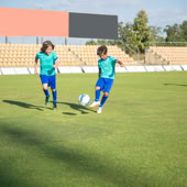 Children playing football on a sunny day in a Portuguese stadium.